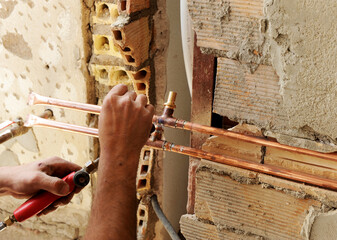 The hands of a plumber while soldering to connect copper pipes during the renovation of the water supply installations in a house.