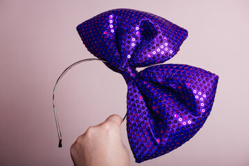 Hand holding a large glittery purple bow headband on a pink background.