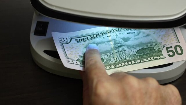 Examination of american dollar (USD) cash money with UV counterfeit detector. Concept of authenticity check, fight against counterfeiting of banknotes, anti fraud measures in USA. Close up view.