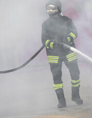 Firefighter with fire hose in middle of smoke of fire during extinguishing