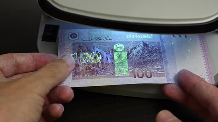 Examination of malaysian ringgit (MYR) cash money with UV counterfeit detector. Concept of authenticity check, fight against counterfeiting of banknotes, anti fraud measures in Malaysia. Close up view
