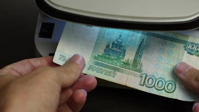 Examination of russian ruble (RUB) cash money with UV counterfeit detector. Concept of authenticity check, fight against counterfeiting of banknotes, anti fraud measures in Russia. Close up view.