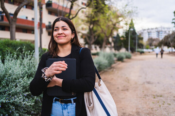 Young influencer walking in a park, holding her tablet and smiling, enjoying a sunny day