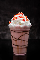 Strawberry milkshake with chocolate syrup in clear glass on dark background.