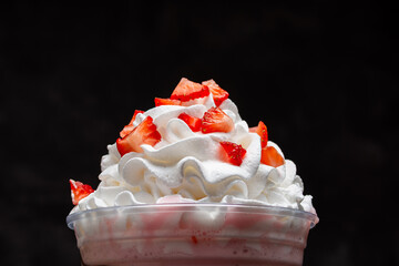 Strawberry milkshake with chocolate syrup in clear glass on dark background.