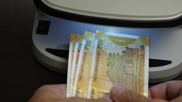 Examination of indian rupee (INR) cash money with UV counterfeit detector. Concept of authenticity check, fight against counterfeiting of banknotes, anti fraud measures in India. Close up view.