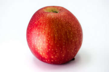 Fresh red apple sits on a white surface, showcasing its vibrant color and smooth texture in natural light