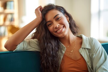 Fototapeta premium A young woman with long curly hair smiles while sitting on a teal couch