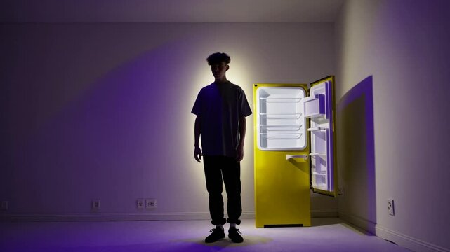  Homme fig&eacute; face &agrave; un frigo jaune ouvert dans une pi&egrave;ce vide