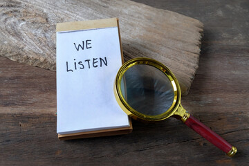 We listen text written on a notebook and magnifying glass.