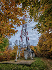 A close-up side view of the Kis-kőhát radio tower and its utility building, surrounded by vivid...