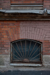 Rusty iron bars cover an arched basement window set in aged brick