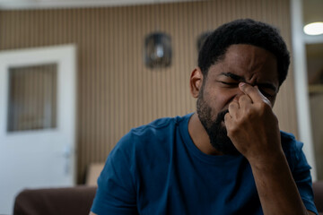 Black man at home suffering from headache and visible migraine pain, stressed and unwell in living room.