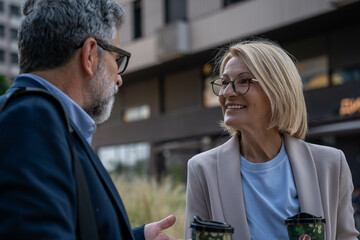 Businesswoman and businessman talking outdoors, close-up conversation, smiling faces, cheerful...