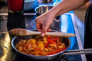 A close-up, high-detail macro shot capturing a woman preparing chicken sauté, showcasing sizzling ingredients, textures, and cooking action in a warm kitchen environment.