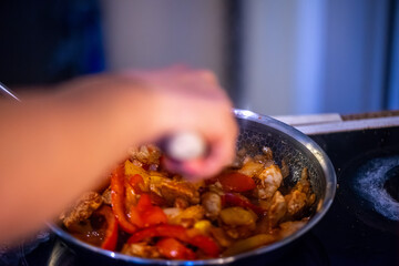 A close-up, high-detail macro shot capturing a woman preparing chicken sauté, showcasing sizzling ingredients, textures, and cooking action in a warm kitchen environment.