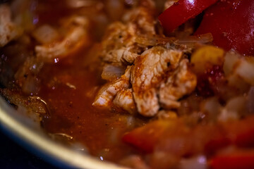 A close-up, high-detail macro shot capturing a woman preparing chicken sauté, showcasing sizzling ingredients, textures, and cooking action in a warm kitchen environment.