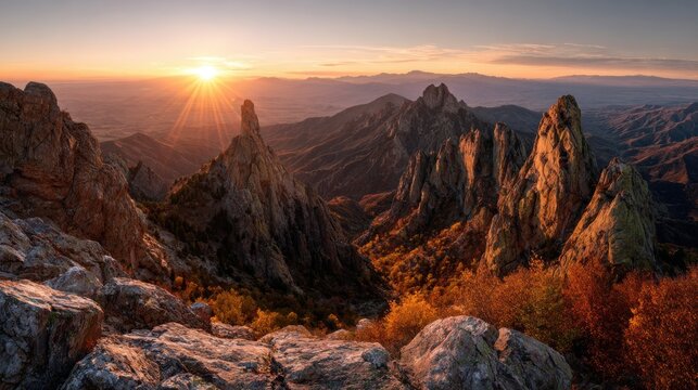 Dramatic sunrise illuminates jagged mountain peaks and autumn foliage in a rugged landscape