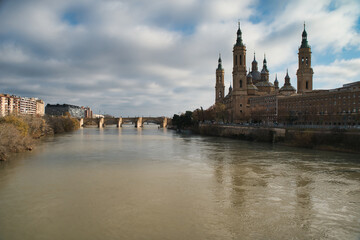 The image shows the Stone Bridge over the Ebro River in Zaragoza, Spain, with the Basilica of Our Lady of the Pillar in the background.