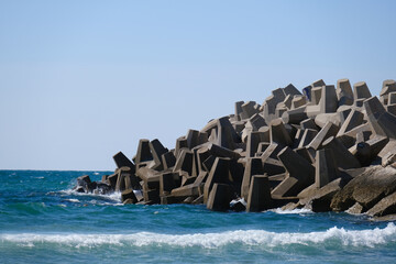 Concrete wave breaker tetrapods protecting the shoreline from strong sea waves under a clear blue...