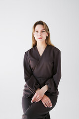 Portrait of a young female doctor or cosmetologist in brown medical uniform, posing confidently on white background.