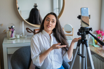 A young woman is filming a video on her phone for a blog in her room. Social media. Online life.