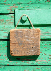 Blank wooden sign hanging on rustic wall in sunlight