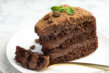 Piece of delicious chocolate cake with coffee beans, mint and fork on light table, closeup