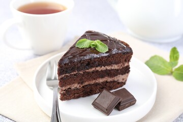 Piece of delicious chocolate cake, mint and fork on light table, closeup
