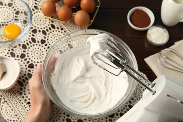 Woman whisking cream with hand mixer at table, top view
