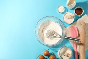 Whisk with whipped cream, eggs and other products on light blue table, flat lay. Space for text