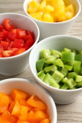 Pieces of fresh colorful bell peppers in bowls on wooden table, closeup