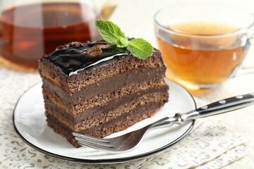 Piece of chocolate cake served with mint, fork and tea on table, closeup