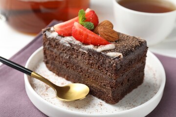 Piece of delicious chocolate cake with strawberry, almonds and tea on table, closeup