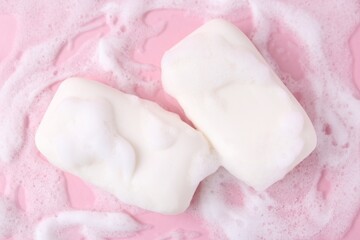 Soap bars with foam on pink background, flat lay