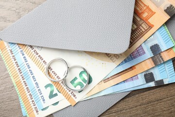 Silver wedding rings, envelope and euro banknotes on wooden table, flat lay