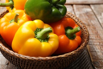 Fresh colorful bell peppers in wicker basket on wooden table, closeup