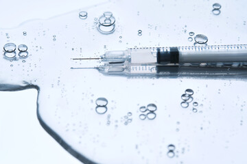 A syringe for injection in an appetizing drop with bubbles. Blue steel background.