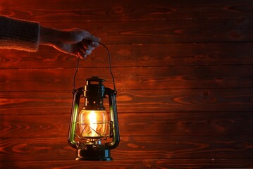 Woman holding vintage kerosene lantern near wooden wall, closeup. Space for text