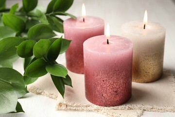 Burning candles and green leaves on white table, closeup