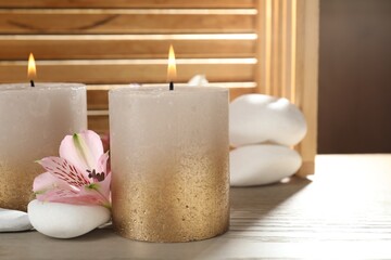 Burning candles, stones and lily flowers on wooden table, closeup