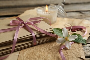 Stack of love letters, flower, candle and parchment sheets on wooden table, closeup