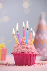 Burning candles in cupcake, sprinkles and party decor on table against blurred lights