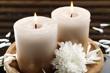 Burning candles and beautiful flowers on wet black mirror surface, closeup