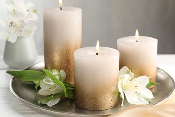 Burning candles and beautiful flowers on white table, closeup
