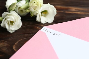 Letter with phrase I Love You, envelope and beautiful flowers on wooden table, closeup