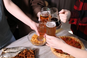 Friends clinking glasses of beer at white wooden table, closeup
