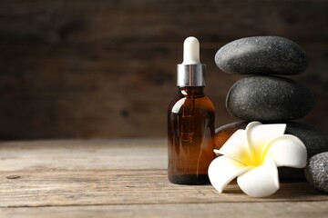 Spa stones, cosmetic product and plumeria flower on wooden table, closeup. Space for text