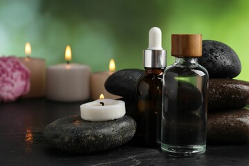 Spa composition with wet stones, cosmetic products and burning candles on dark textured table against blurred green background, selective focus