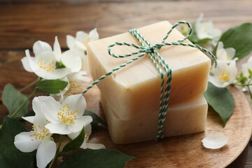 Soap bars and jasmine flowers on wooden table, closeup